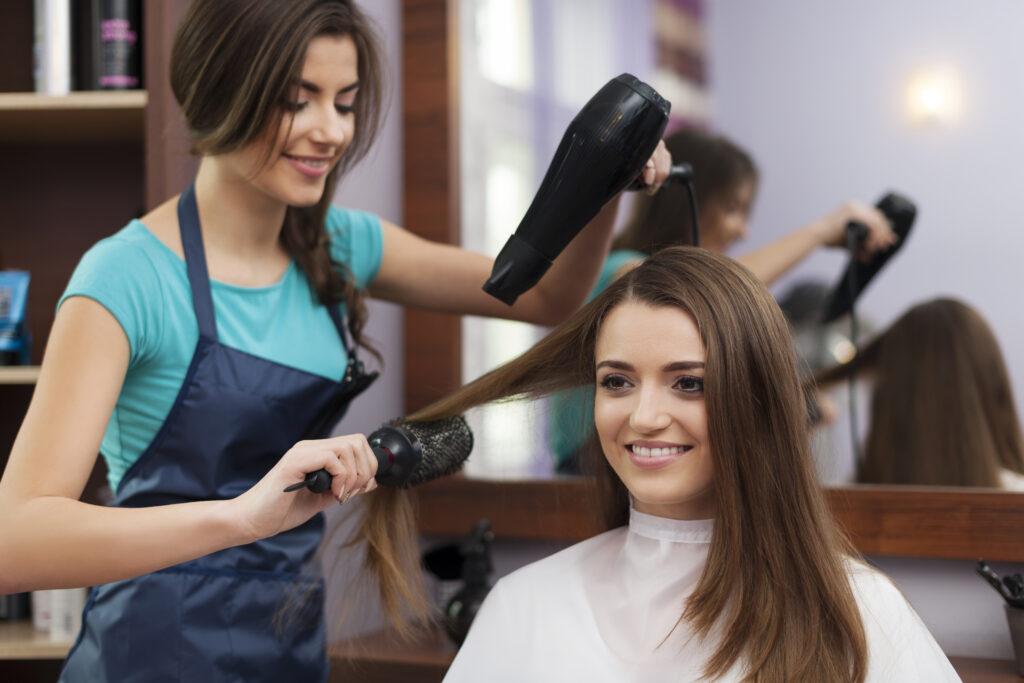 Female hairdresser using hairbrush and hair dryer in women salon