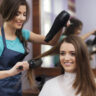 Female hairdresser using hairbrush and hair dryer in women salon